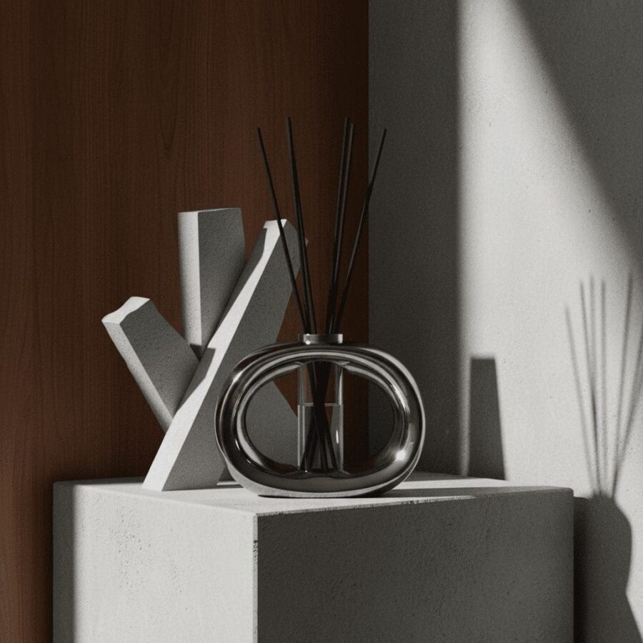 Silver oval porcelain reed diffuser on geometric stone pedestal with architectural shadows.